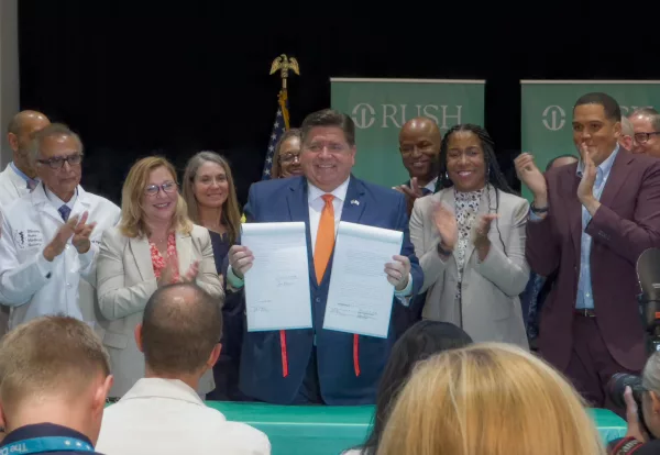 Gov. JB Pritzker holds up a pair of bills that were part of the Healthcare Protection Act, which he signed into law Wednesday at Rush University Medical Center in Chicago. Pritzker first outlined the insurance changes in his State of the State address in February. (Capitol News Illinois photo by Dilpreet Raju)