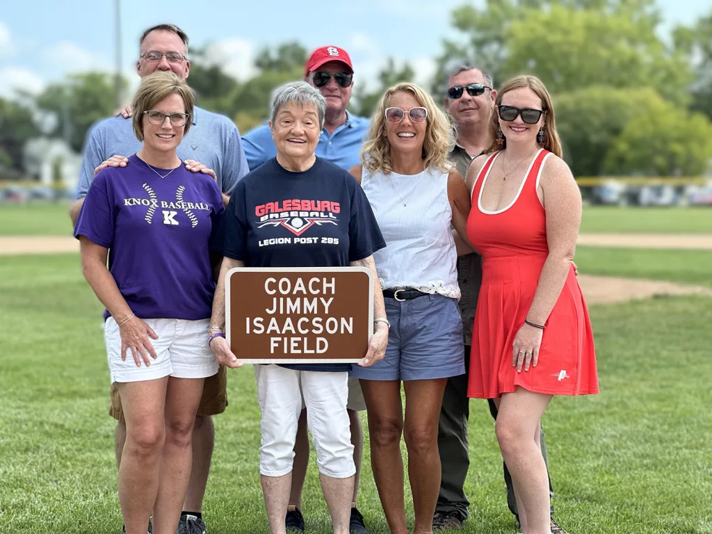 The family of Jimmy Isaacson pose with a replica sign that will be displayed at the baseball diamond at H.T. Custer Park. Holding the sign his his wife Pat. To her left is daughter Amy, and in the middle in the back row is son Jami
