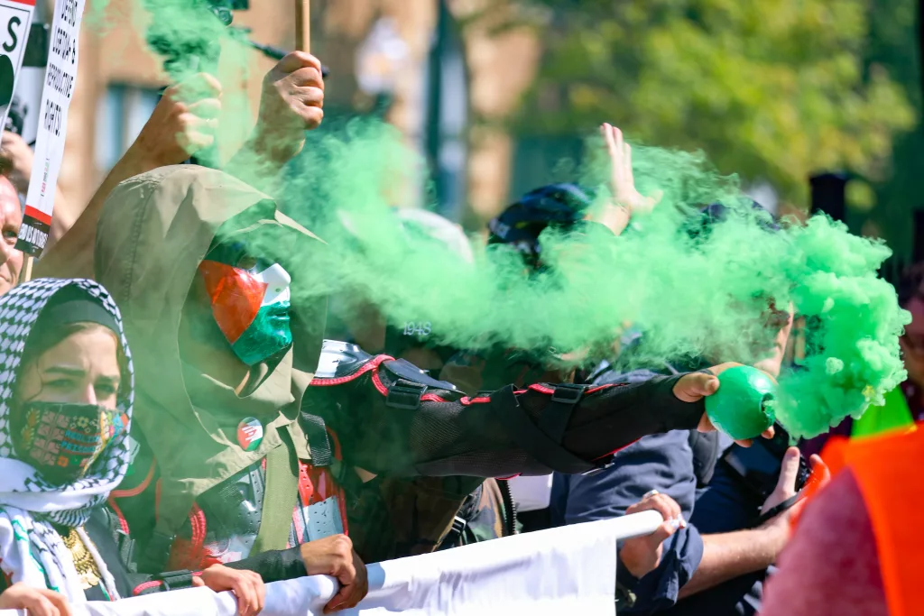 A masked protestor holds up a green smoke bomb during a protest march on Monday near the site of the Democratic National Convention in Chicago. (Capitol News Illinois photo by Andrew Adams)