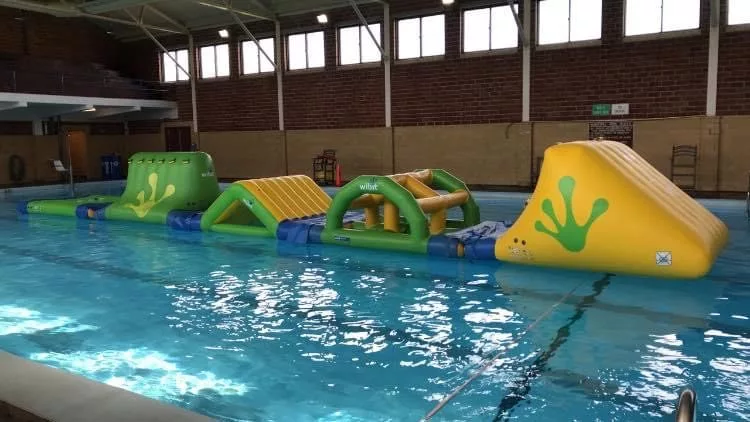 Image of indoor pool with yellow and green inflatable obstacle course