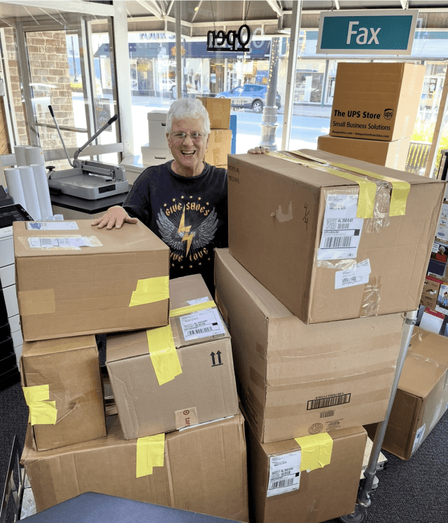 older woman pictured with boxes at the UPS Store, full of donated shoes