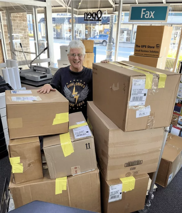 older woman pictured with boxes at the UPS Store, full of donated shoes