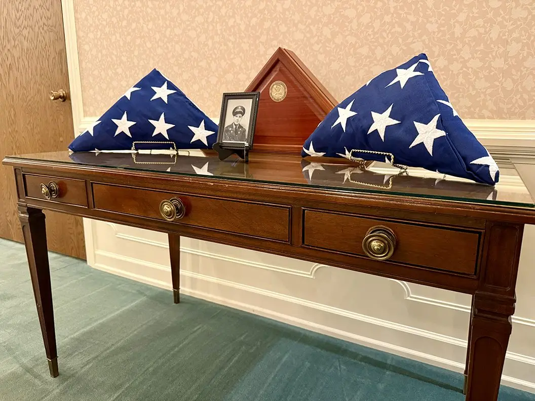 A military photo of Cpl. Paul Hoots and two American flags rest on a table during funeral services for the fallen Korean War hero on Thursday, July 24, 2025, at Hinchliff-Pearson-West Funeral Directors in Galesburg. (JAY REDFERN/WGIL)