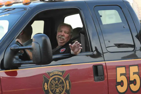 Tom “Baughie” Baughman smiles and waves from the window of a Galesburg Fire Department rescue truck. Courtesy photo by Bill Dickerson.