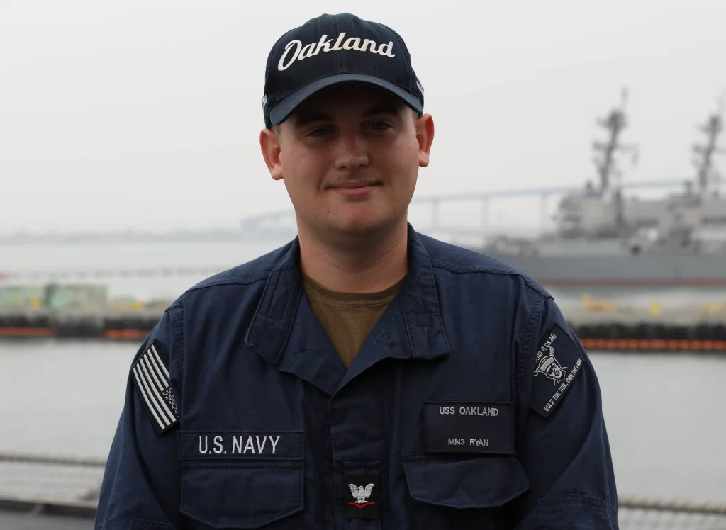 U.S. Navy Petty Officer 3rd Class Kolby Ryan, a 2021 Knoxville High School graduate, stands aboard USS Oakland while wearing an Oakland ball cap and navy working uniform. (Photo: U.S. Navy)
