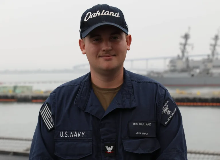 U.S. Navy Petty Officer 3rd Class Kolby Ryan, a 2021 Knoxville High School graduate, stands aboard USS Oakland while wearing an Oakland ball cap and navy working uniform. (Photo: U.S. Navy)