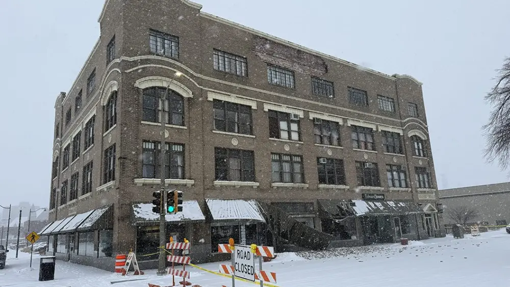 Wide view of Weinberg Arcade building in downtown Galesburg with caution tape, road closed sign, and scattered bricks after facade collapse.