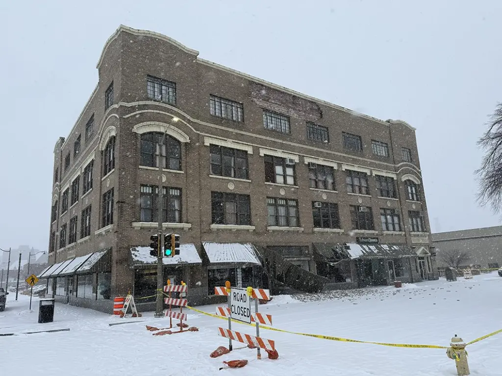 Wide view of Weinberg Arcade building in downtown Galesburg with caution tape, road closed sign, and scattered bricks after facade collapse.