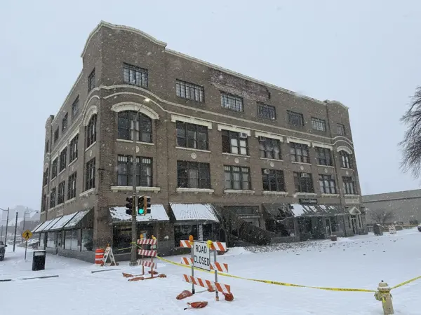Wide view of Weinberg Arcade building in downtown Galesburg with caution tape, road closed sign, and scattered bricks after facade collapse.