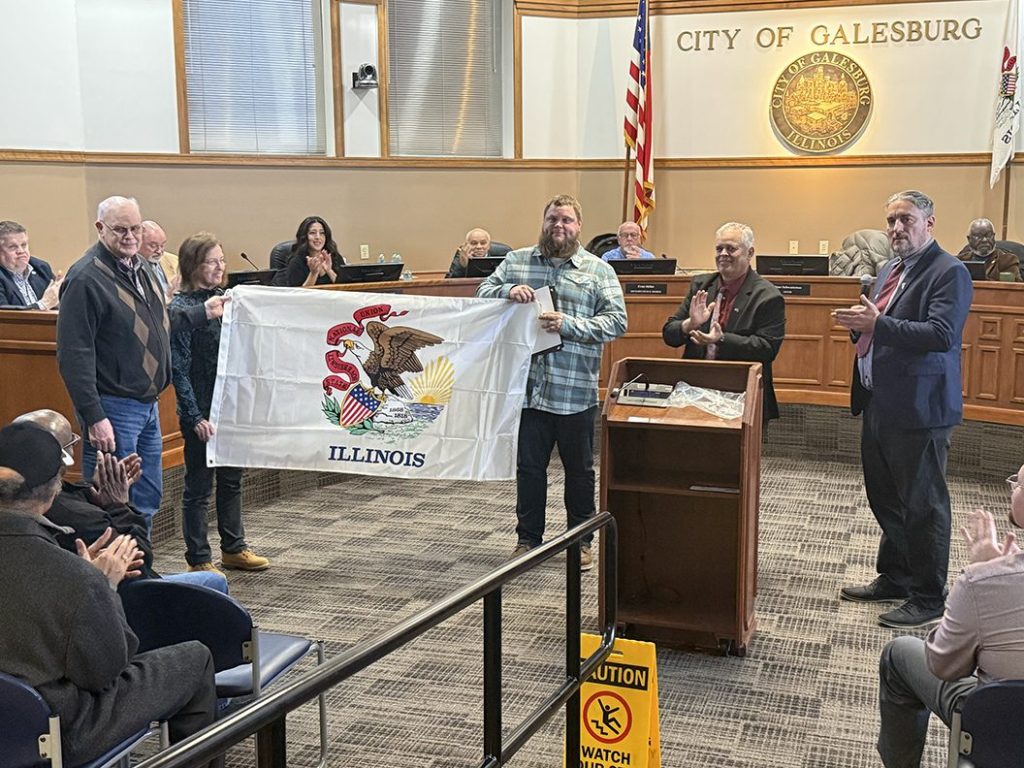 Veteran Byron Baird with parents Doug and Nancy Baird and Rep. Dan Swanson holding Illinois flag at Galesburg City Council veteran honor ceremony