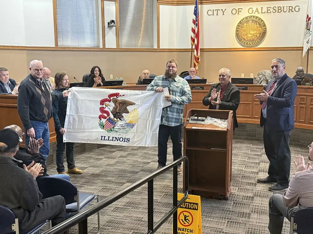 Veteran Byron Baird with parents Doug and Nancy Baird and Rep. Dan Swanson holding Illinois flag at Galesburg City Council veteran honor ceremony