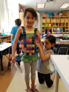 Young girl wearing colorful Lux Blox creation in classroom