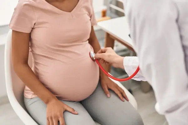 Doctor listens to a pregnant woman’s abdomen using a stethoscope. (Photo Credit: Krakenimages.com, adobe stock)