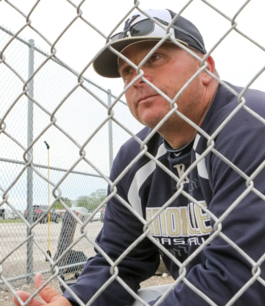 Knoxville baseball coach Rick Reed peering intently through the dugout fence during a game