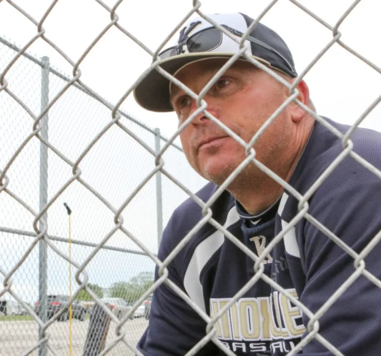 Knoxville baseball coach Rick Reed peering intently through the dugout fence during a game