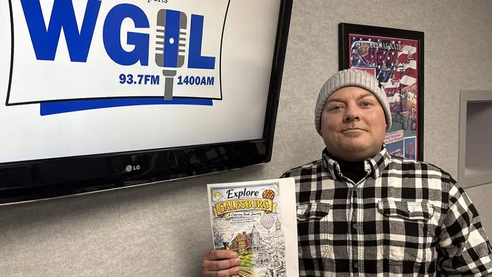 Derek Peters holding Explore Galesburg coloring book cover at WGIL studios