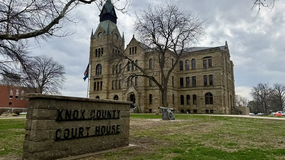 Knox County Courthouse sign in foreground with the historic stone courthouse building behind it in Galesburg, Illinois