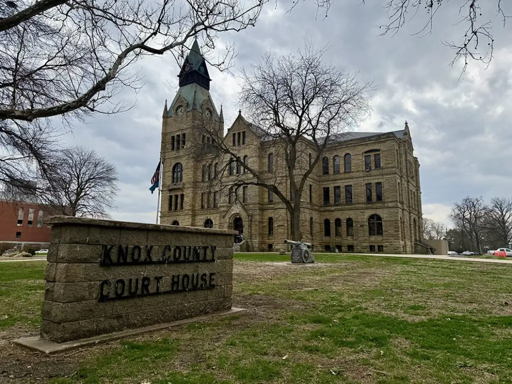 Knox County Courthouse sign in foreground with the historic stone courthouse building behind it in Galesburg, Illinois