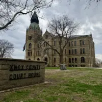 Knox County Courthouse sign in foreground with the historic stone courthouse building behind it in Galesburg, Illinois