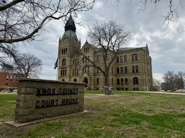 Knox County Courthouse sign in foreground with the historic stone courthouse building behind it in Galesburg, Illinois