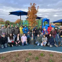 Volunteers gather around a newly planted Fall Fiesta Sugar Maple at Cooke Park in Galesburg, Illinois, during a 2025 tree planting event.
