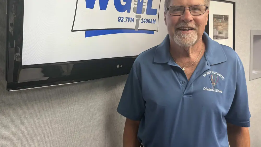 ALT TEXT: Greg Saul, wearing a Great Balloon Race polo shirt, standing in the WGIL studio.