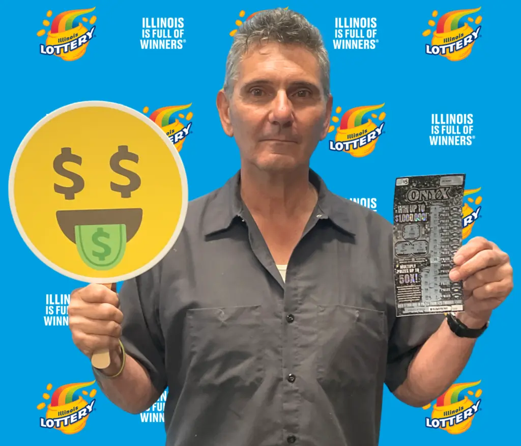 A man holding a lottery ticket and a dollar-sign emoji prop, standing in front of an Illinois Lottery backdrop.