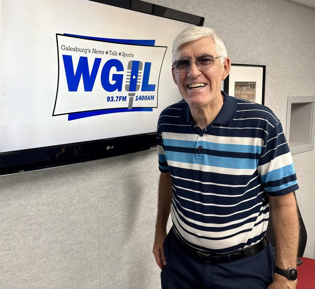 Jim Reinebach smiling in front of the WGIL logo at the station's Galesburg studios.