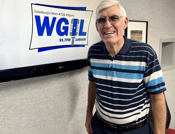 Jim Reinebach smiling in front of the WGIL logo at the station's Galesburg studios.