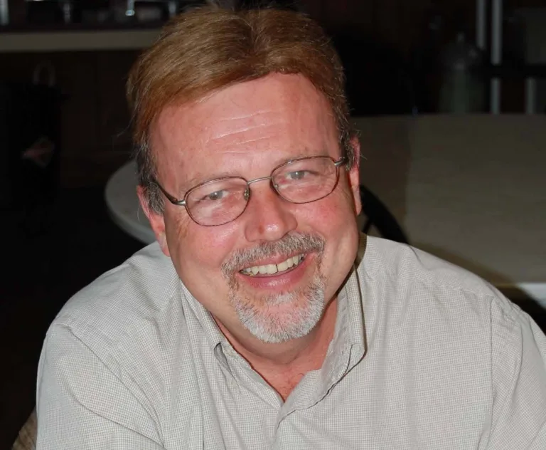 Doug Ferreter smiling, wearing glasses and a checkered button-down shirt
