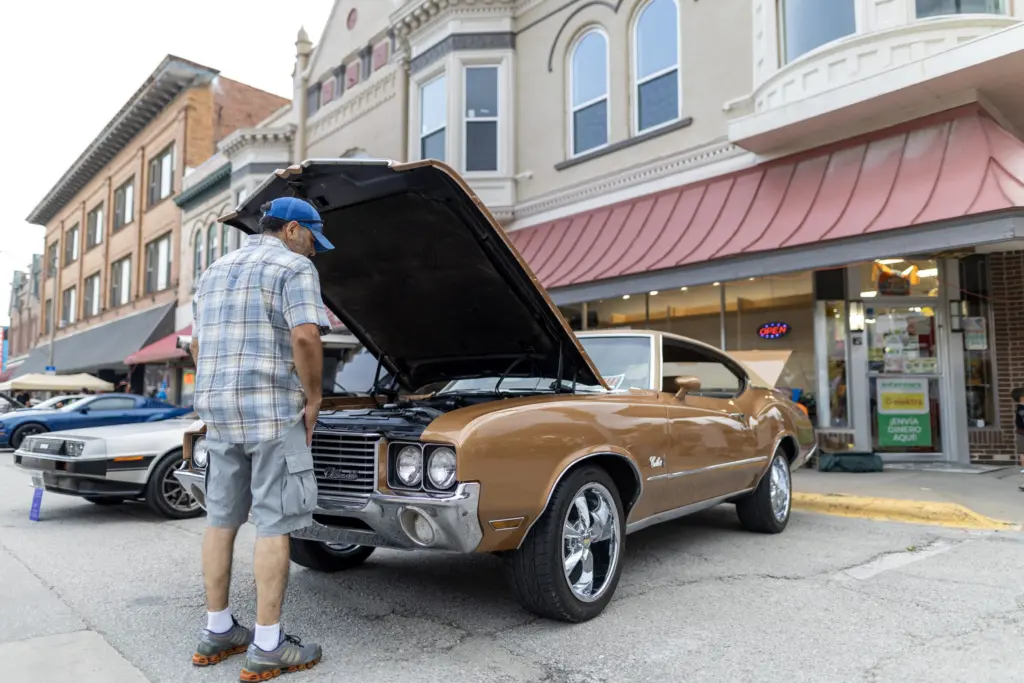 Man looking under the open hood of a gold Oldsmobile Cutlass