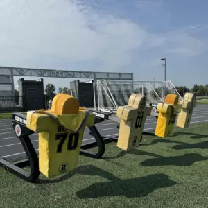 ALT TEXT: Football blocking sleds with padded dummies on the turf at CBI Bank & Trust Stadium