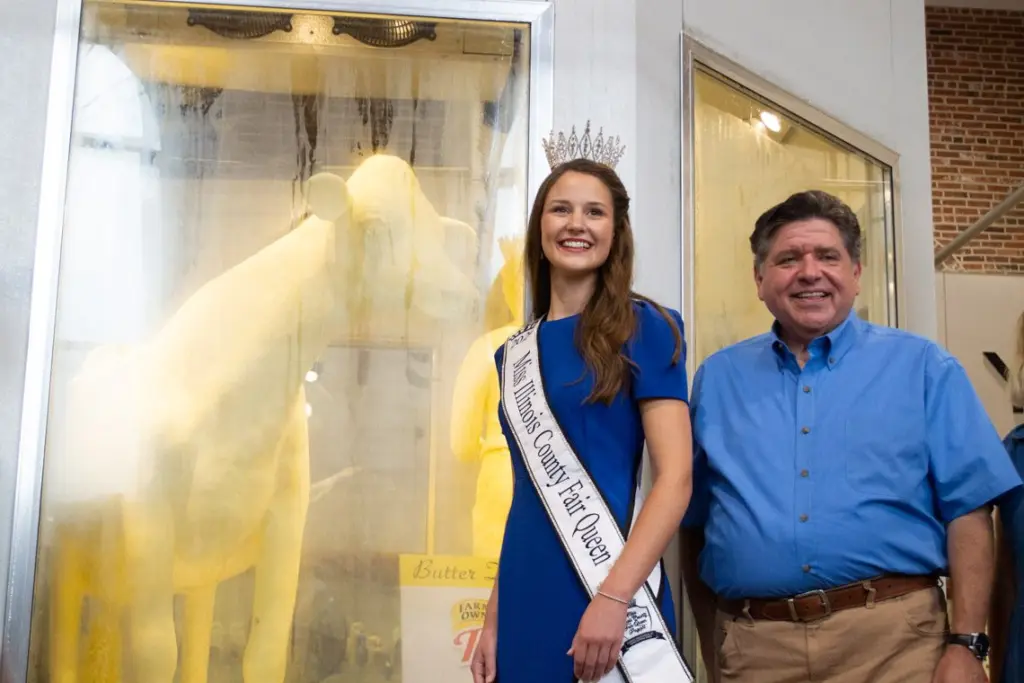 Illinois State Fair Quen Krista Phillips and Gov. JB Pritzker pose with the 2026 Illinois State Fair butter cow. (Capitol News Illinois photo by Jerry Nowicki)