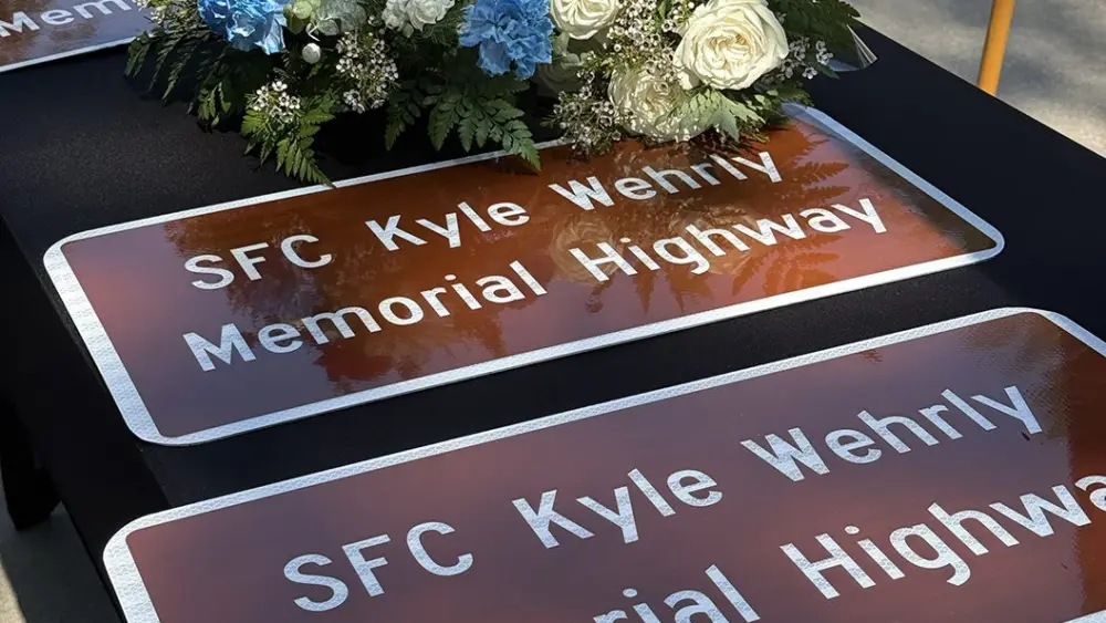 ALT TEXT: Two SFC Kyle Wehrly Memorial Highway signs on a table with a floral arrangement