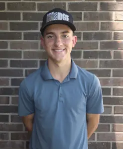 Aidan Nelson wearing a golf polo and cap in front of a brick wall