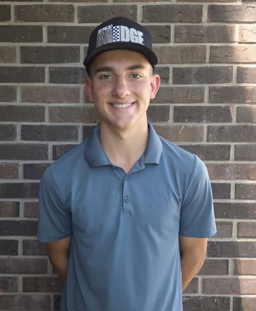 Aidan Nelson wearing a golf polo and cap in front of a brick wall