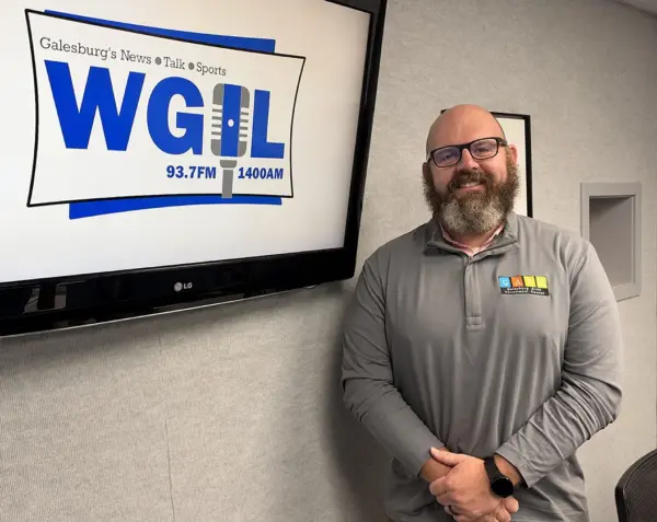 Adam Seaney standing in front of the WGIL logo in the station's studio