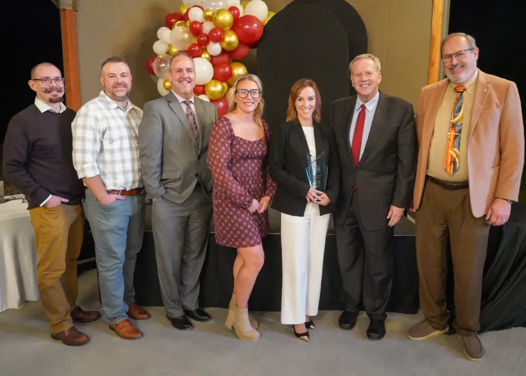 Seven people posing together, one holding a glass Large Business Excellence award, at a Chamber of Commerce awards event