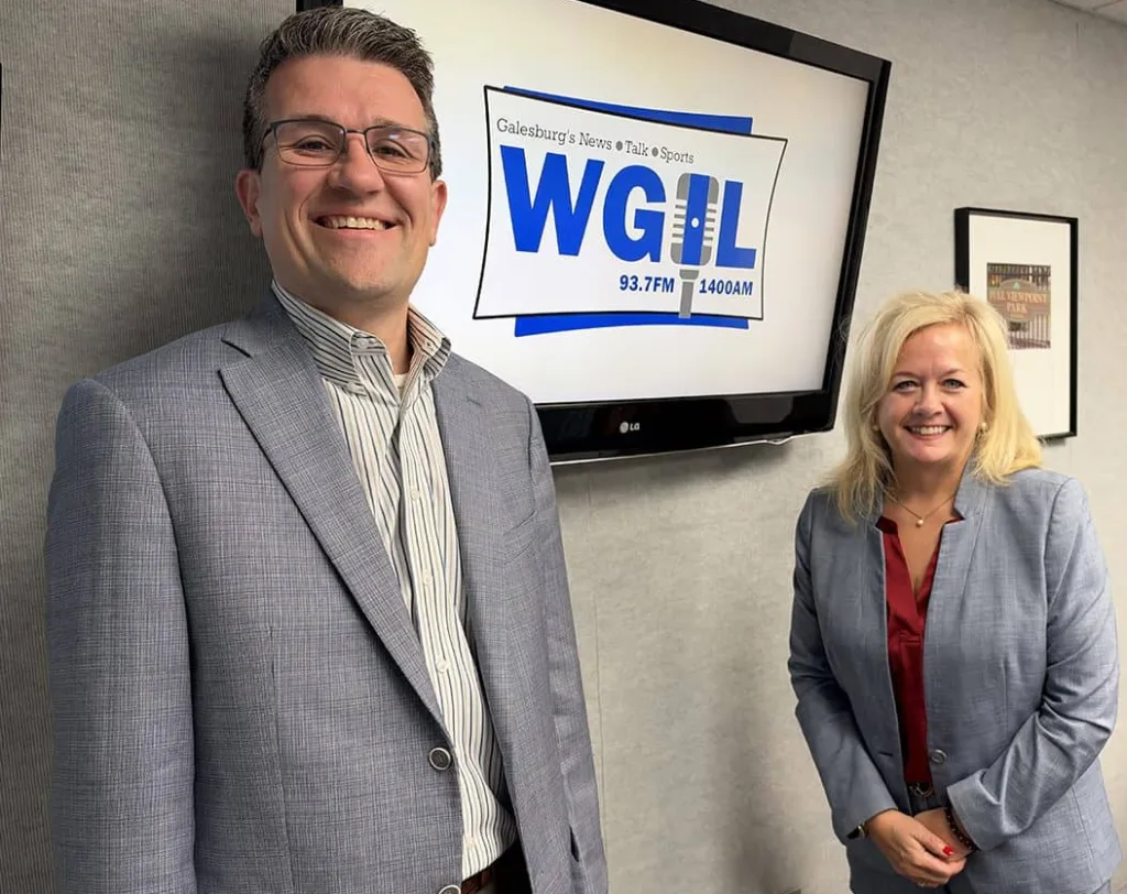 Josh Gibb and DeAnne Bloomberg stand beside a screen displaying the WGIL logo