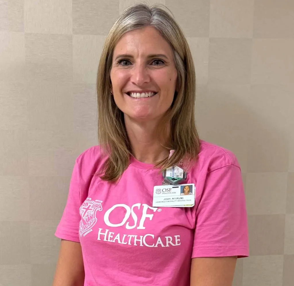 Jody Henry smiles in a pink OSF HealthCare T-shirt with an OSF badge clipped to the collar