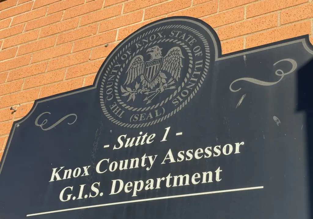 Black sign with the Knox County, Illinois, seal reading "Suite 1 – Knox County Assessor, G.I.S. Department" on a brick wall