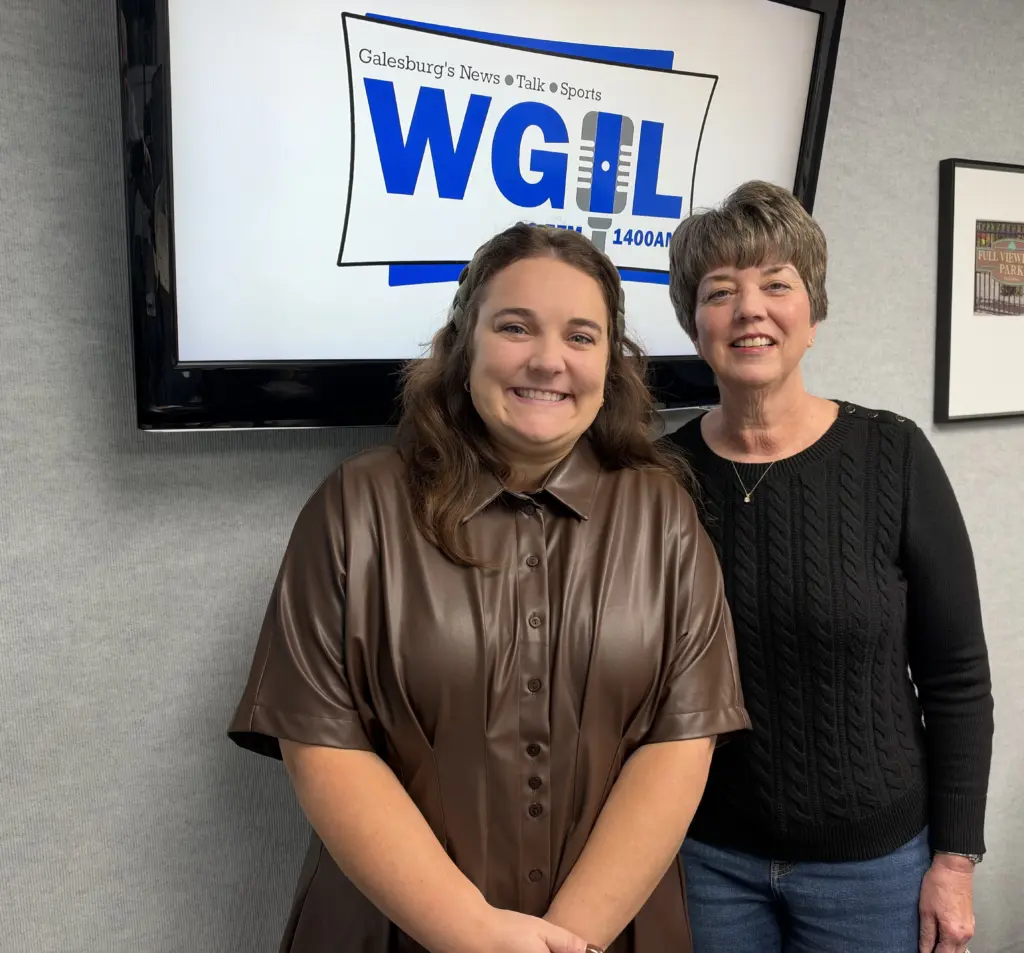 Two women smile in front of a screen showing the WGIL logo in the station’s studio.