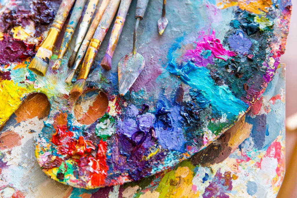 Closeup of art palette with bright colorful mixed paints, paintbrushed and palette knives