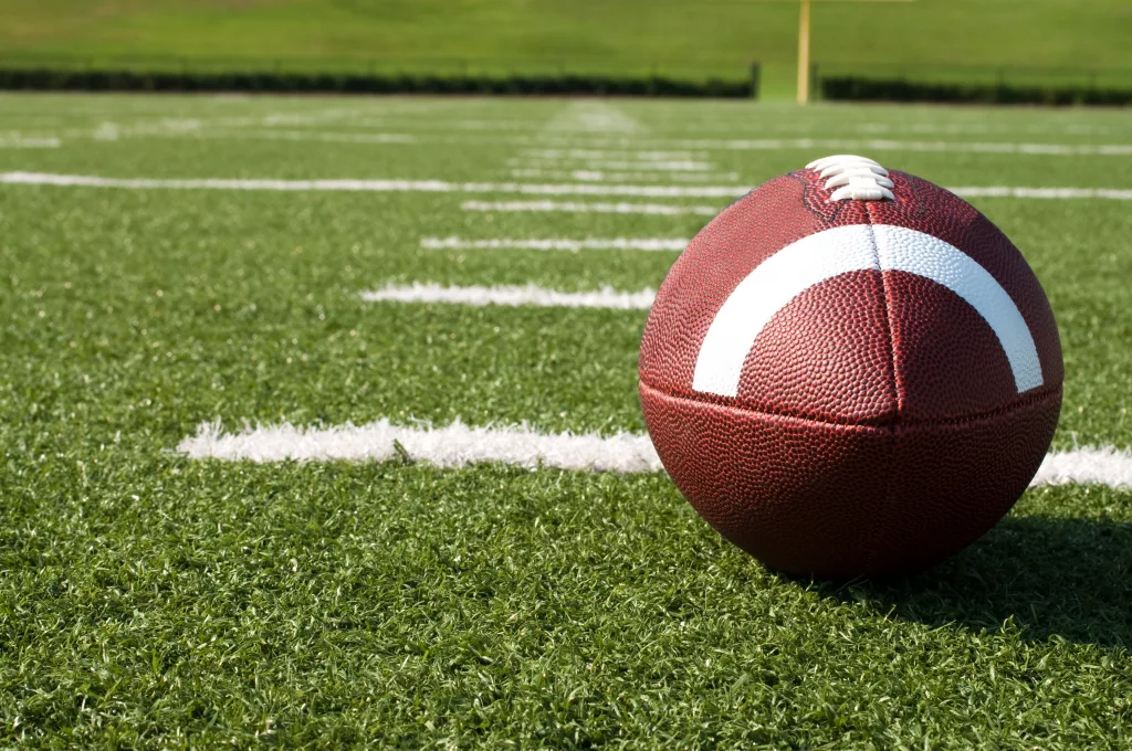 Closeup of American football on field with yard lines.