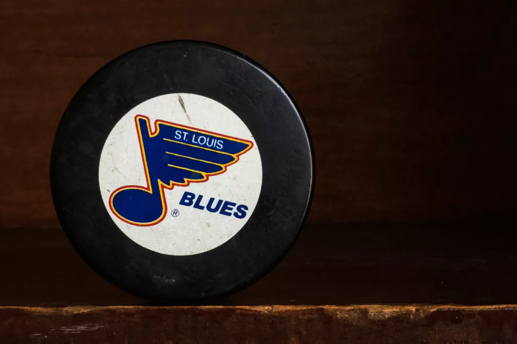 A hockey puck bearing the logo of the St. Louis Blues professional hockey team of the NHL stands on a shelf in a still life image.