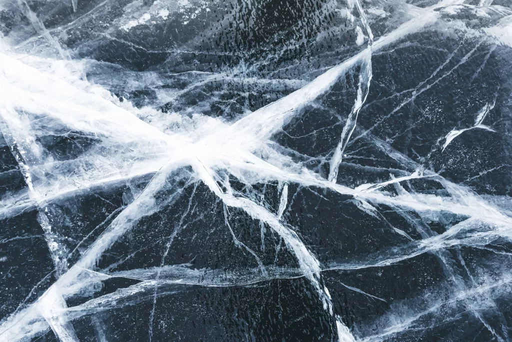 Crack in the ice on a frozen lake covered with snow. Cracked black ice texture background