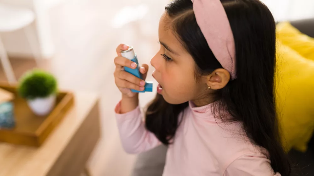 Side view of a cute little girl with breathing problems using an asthma inhaler