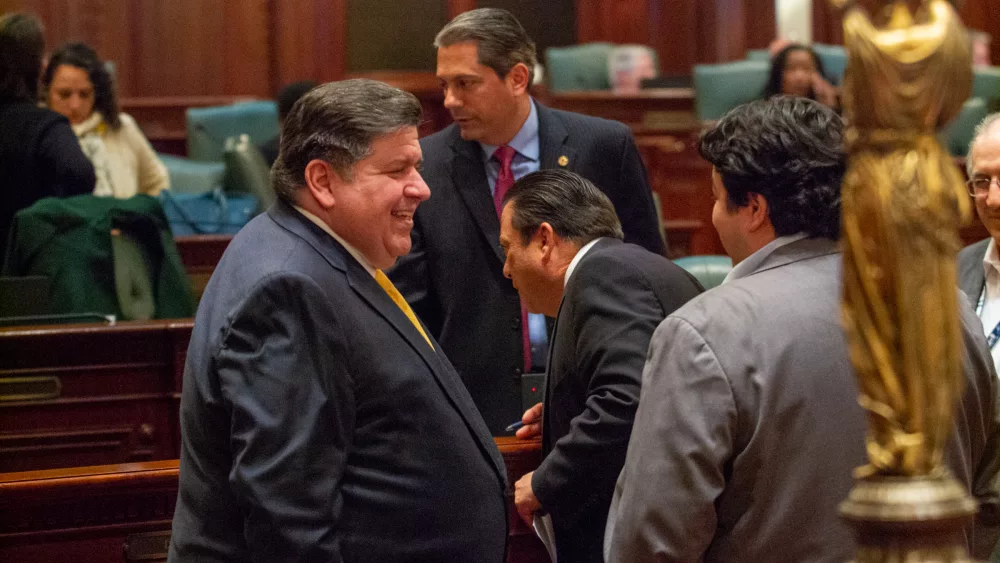 Gov. JB Pritzker talks with members of the Illinois House prior to a vote on his initiative to reform the state’s insurance industry. (Capitol News Illinois photo by Jerry Nowicki)