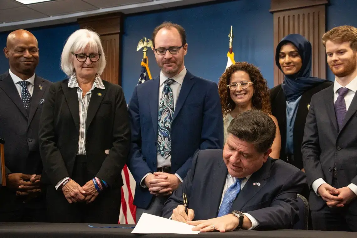 Gov. JB Pritzker signs the Artificial Intelligence Safety Measures Act into law in Chicago on July 6, 2026, surrounded by lawmakers and advocates. (Capitol News Illinois photo by Maggie Dougherty)