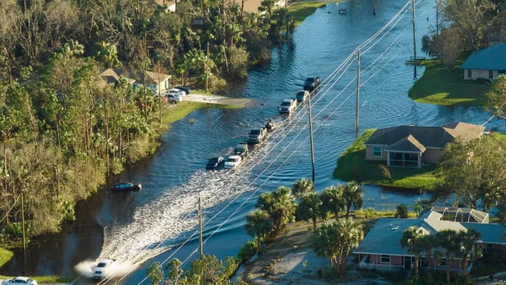 Hurricane flooded street with moving cars and surrounded with water houses in Florida residential area.